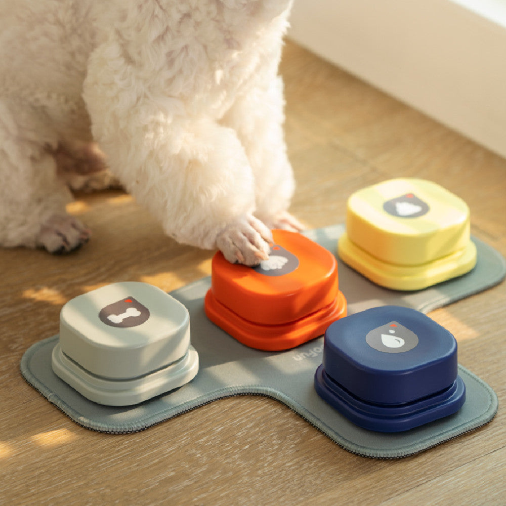 Colorful dog toys on a mat with a dog pawing at one of them on a wooden floor.